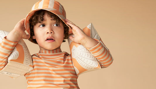 Remy pulls on the KIDLY Label Recycled Bucket Hat in Apricot Shell/Stripe, to match his Recycled Rash Vest and Swimming Armbands